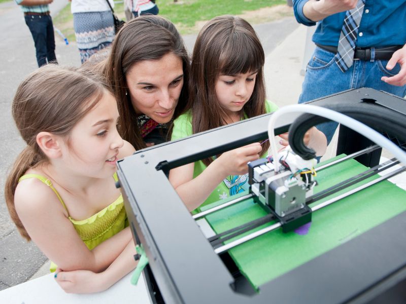An adult with two children staring and examining a 3D printer. 